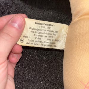 K&ouml;nnte beinhalten: Nahaufnahme eines Cabbage Patch Kids Puppenetiketts. Das Etikett ist wei&szlig; mit schwarzem Text, einschlie&szlig;lich der Copyright-Informationen f&uuml;r 1978 und 1982. Das Etikett enth&auml;lt auch die Informationen des Herstellers und Waschanweisungen.