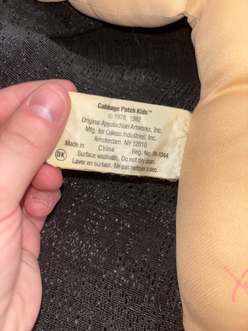 K&ouml;nnte beinhalten: Nahaufnahme eines Cabbage Patch Kids Puppenetiketts. Das Etikett ist wei&szlig; mit schwarzem Text, einschlie&szlig;lich der Copyright-Informationen f&uuml;r 1978 und 1982. Das Etikett enth&auml;lt auch die Informationen des Herstellers und Waschanweisungen.