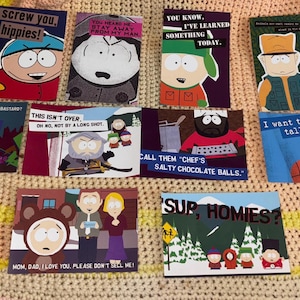 May include: A collection of colorful South Park-themed greeting cards. Each card features characters and phrases from the show, including "Screw you, hippies!" and "I want to be tall and black." The cards are displayed on a patterned blanket.