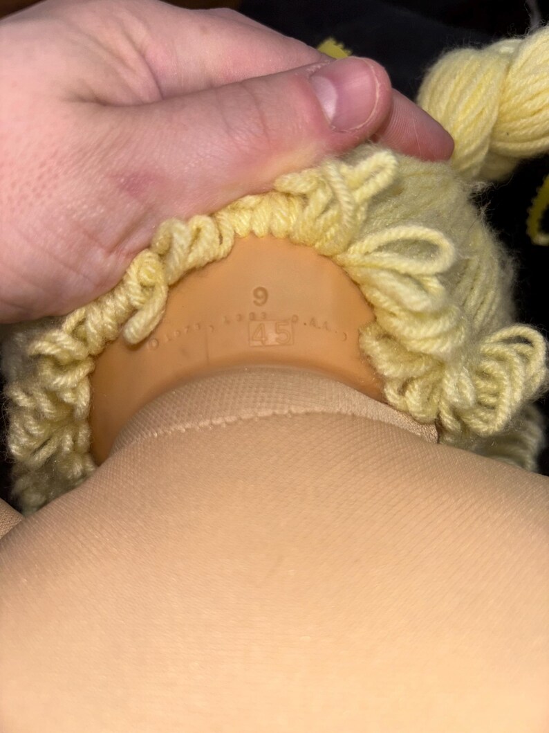 K&ouml;nnte beinhalten: Ein Puppenkopf mit gelber Garnper&uuml;cke und einem hellbraunen K&ouml;rper. Der Puppenkopf besteht aus hellbraunem Kunststoff. Die Per&uuml;cke ist mit Locken und Z&ouml;pfen versehen. Die Zahlen "9" und "45" sind auf der R&uuml;ckseite des Kopfes aufgedruckt.