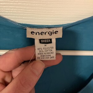 May include: A blue sheer top with a white tag that reads "energie SHEER M 65% POLYESTER 35% COTTON MADE IN MACAU AN# 33364 SEE SIDE FOR CARE"