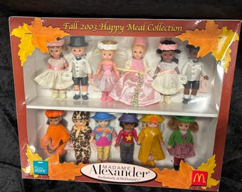 May include: A boxed set of Madame Alexander dolls from the Fall 2003 Happy Meal Collection. The dolls are dressed in various outfits, including dresses, suits, and raincoats. The box features fall leaf accents and the McDonald's logo.