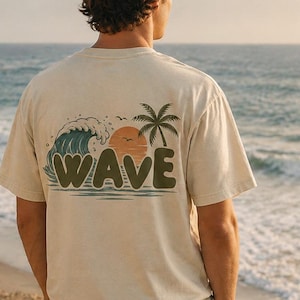Peut inclure: Un t-shirt beige avec un motif vague rétro représentant une vague bleue, un soleil orange et un palmier. Le mot "WAVE" est imprimé en gras, en vert. Le t-shirt est porté par une personne sur une plage face à l'océan.