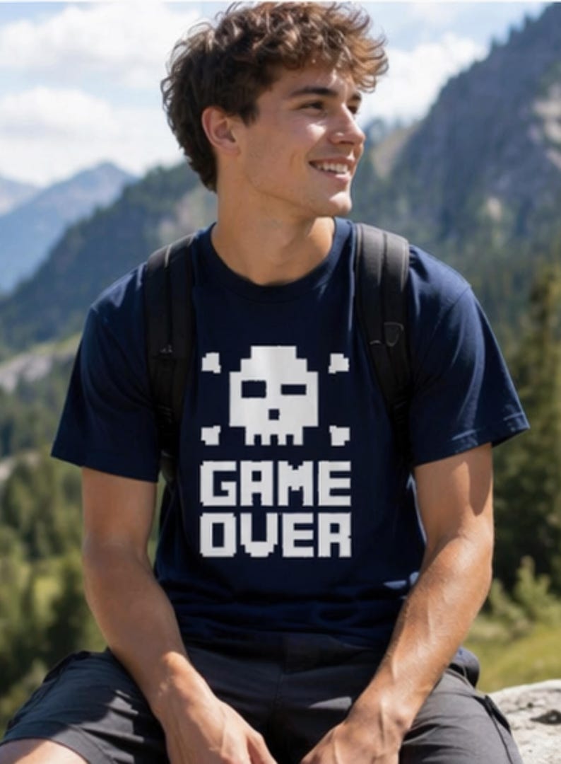Pode incluir: Camiseta azul marinho com um design de caveira e ossos cruzados pixelizados em branco e a frase "GAME OVER". A camiseta &eacute; feita de um material macio e &eacute; adequada para roupas casuais.