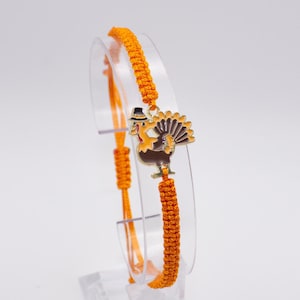 May include: Orange macrame bracelet with a gold turkey charm. The charm has a black hat and brown and white feathers.  AVAILABLE IN 13 COLORS!