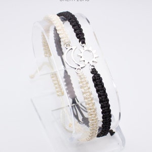 May include: Two friendship bracelets with a silver sun and moon charm. The bracelets are black and white.