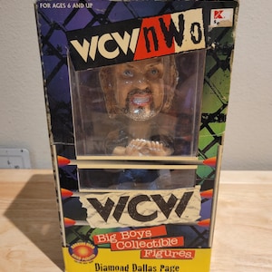 May include: A boxed Diamond Dallas Page action figure from the WCW Big Boys Collectible Figures line. The box is yellow, black, and red with a picture of the figure inside. The figure is a bobblehead with a black beard and a blue shirt.
