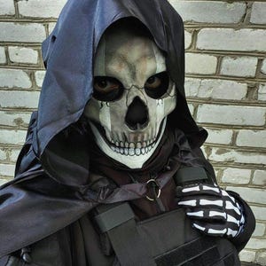 May include: A person wearing a skull mask with a black hood and tactical vest. The vest has the text "Ukr.Ghost" on it. The person is also wearing skeleton gloves.