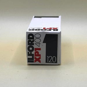 May include: A white box of Ilford XP1 400 film. The box has black and red text that reads "ILFORD XP1 400" and "120". The number 1 is printed in black on the right side of the box.