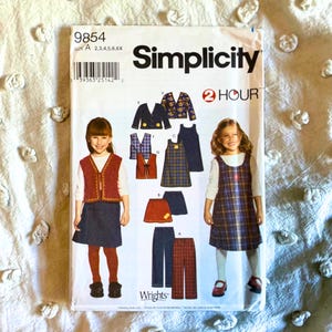 May include: A Simplicity sewing pattern envelope 9854, size A, featuring illustrations of children's clothing including vests, skirts, dresses, and pants. The cover displays two children wearing these garments, with the text 2 HOUR and Wrights.