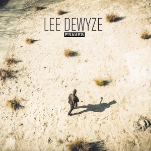 May include: Album cover for "FRAMES" by Lee DeWyze. A person walks across a sandy, desert landscape. The artist's name and album title are displayed in a minimalist font at the top. The image has a muted colour palette, with beige and brown tones.