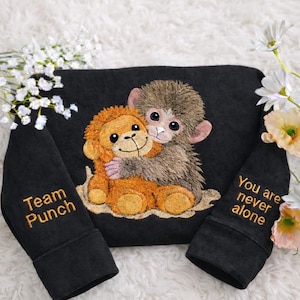 May include: Black sweatshirt featuring an embroidered design of two hugging monkeys. The sleeves have the phrases "Team Punch" and "You are never alone" embroidered in gold. The monkeys are brown and orange.