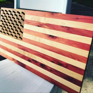 May include: A wooden American flag with red and white stripes. The flag is made of cedar wood and has a brass bullet casing design in the blue field.