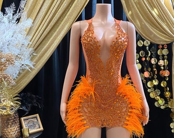 May include: Orange and clear beaded mini dress with a plunging neckline and a feather trim. The dress is on a mannequin.