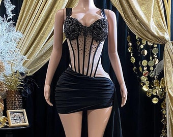 May include: A black corset with a sheer mesh overlay and black bead embellishments. The corset is paired with a black skirt with a high slit and a train.