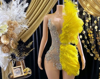May include: A sequined, sheer bodysuit with a yellow feather trim. The bodysuit is on a mannequin in a studio setting.