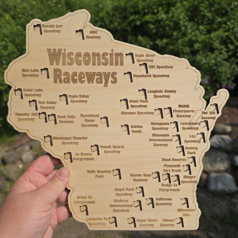 May include: Wooden map of Wisconsin with the words "Wisconsin Raceways" and the names of various speedways. The map is light brown and held by a hand against a green background.
