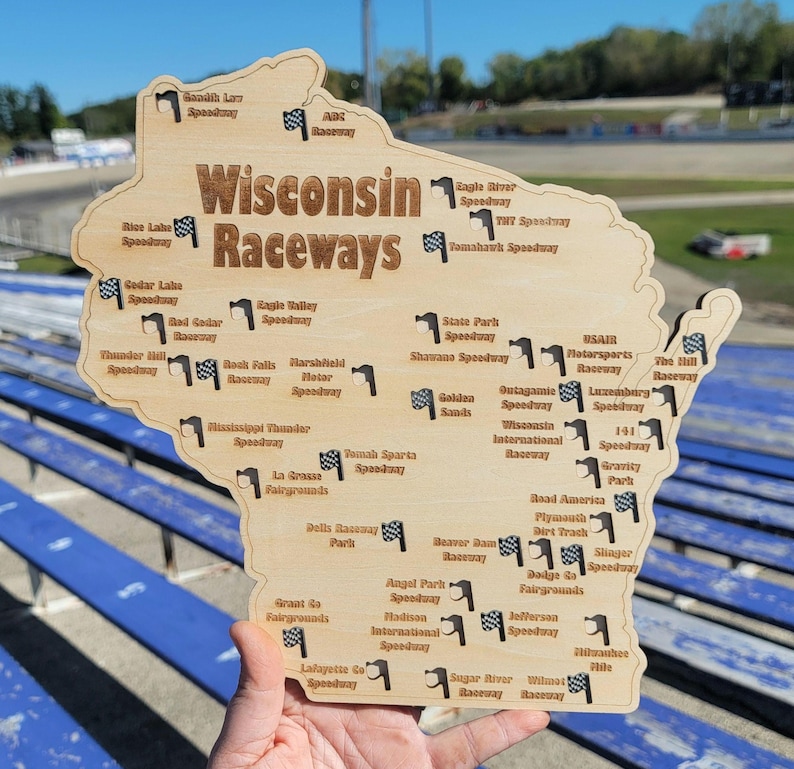 May include: Wooden map of Wisconsin with the text "Wisconsin Raceways" and small checkered flags marking the locations of various speedways. The map is held by a person.