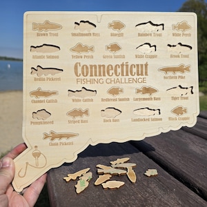 Peut inclure: Puzzle en bois en forme du Connecticut, représentant des espèces de poissons comme la truite brune et l'achigan à grande bouche. Le puzzle est intitulé "Connecticut Fishing Challenge" et comprend des pièces de puzzle en forme de poisson.