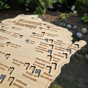 May include: A wooden map of Wisconsin with the text "Wisconsin Raceways" and the names of various speedways. The map is light brown with black text and small flag icons. The map is cut out in the shape of the state.