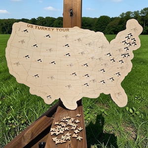May include: Wooden map of the United States with the text "US TURKEY TOUR" at the top. The map has turkey-shaped pins in each state. Small turkey-shaped pins are scattered below the map.
