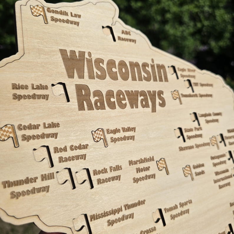 May include: Wooden sign featuring the words "Wisconsin Raceways" with various speedway names and flag graphics. The sign is light brown with dark brown text and graphics, and is shaped like the state of Wisconsin.