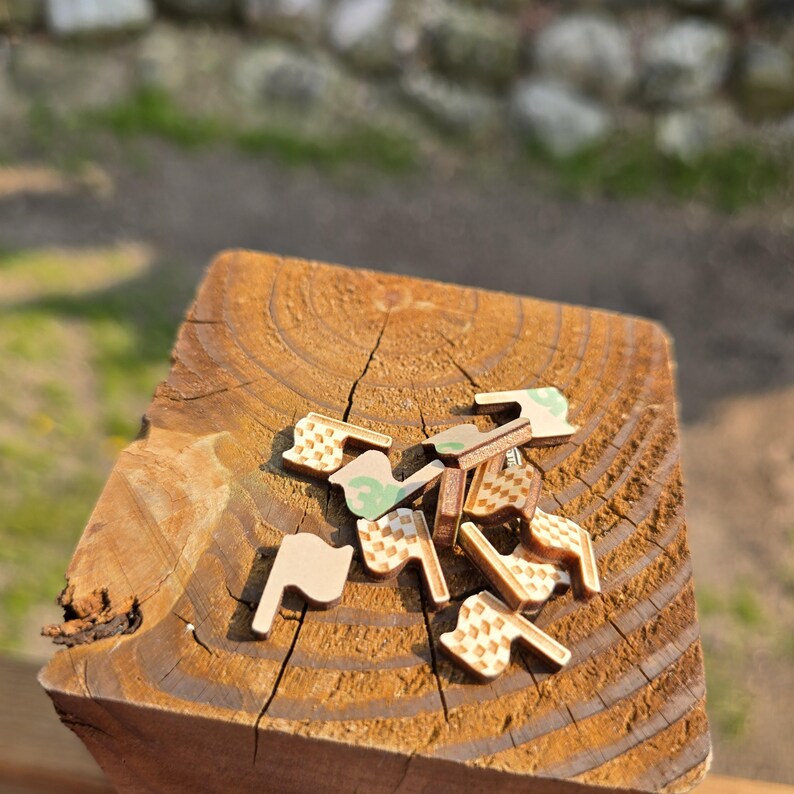 May include: A collection of small, wooden puzzle pieces with various shapes and patterns, including flags and geometric designs. The pieces are scattered on a weathered, brown wooden surface, with a blurred natural background.