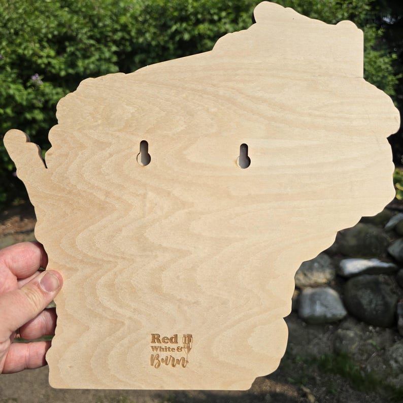 May include: A wooden plaque in the shape of the state of Wisconsin, with two keyhole slots for hanging. The plaque has a light wood grain finish and the words "Red White & Burn" are etched into the lower right corner.