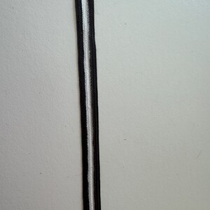 Peut inclure: Gros plan sur un ruban rayé noir et blanc. Le ruban présente une bande blanche centrale flanquée de deux bandes noires. Ce ruban est probablement utilisé pour la couture, l'artisanat ou la décoration.
