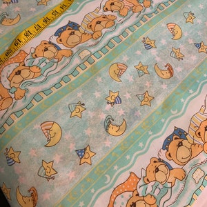 Pode incluir: Tecido azul claro com um padrão repetido de ursinhos dormindo, luas e estrelas. Os ursos usam pijamas e as luas e estrelas têm toucas de dormir. Uma fita métrica amarela está na diagonal sobre o tecido.