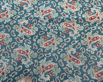 May include: Teal fabric with a repeating paisley pattern in red, white, and light blue. The paisley design is a classic teardrop shape with intricate detailing. A quarter coin is in the image for scale.