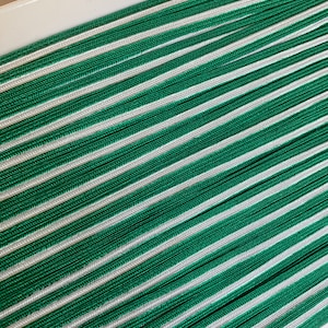 Peut inclure: Gros plan sur des cordons rayés verts et blancs, disposés en diagonale. Les cordons sont tissés serrés, créant une surface texturée. La palette de couleurs est un vert vif associé à un blanc pur.