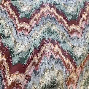 May include: Textile featuring a zigzag design in burgundy, brown, grey, green, and white. The fabric has a textured look with vertical brushstroke-like details. The abstract pattern creates a sense of movement and visual interest.