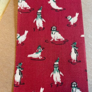 May include: A burgundy necktie featuring a repeating pattern of white seals and penguins. The seals and penguins are wearing green scarves and hats. The tie is made of a woven fabric.