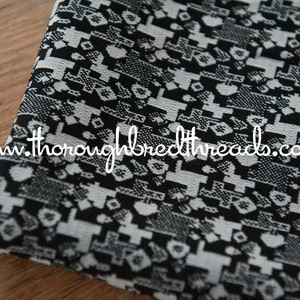 May include: Close-up of a folded fabric with a repeating geometric pattern in black and white. The pattern includes shapes resembling crosses, hearts, and other abstract forms. The website thoroughbredthreads.com is visible.