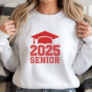 May include: White sweatshirt with red text and a red graduation cap graphic. The text reads "2025 Senior".