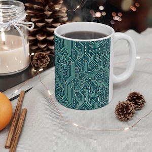 May include: White ceramic mug with a teal blue and green circuit board design. The mug is filled with coffee.