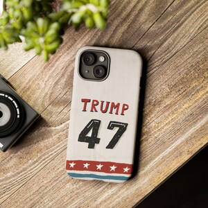 May include: A white iPhone case with a red, white, and blue design. The case features the text "TRUMP 47" in black lettering.