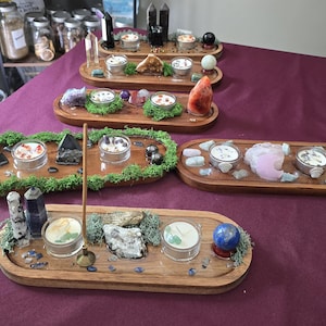 May include: Six oval wooden trays arranged on a dark surface, each featuring embedded green moss, various polished crystals, gemstones, and small glass candle holders. Some trays include incense holders, while others display spheres, points, and raw mineral clusters.