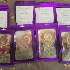 May include: Eight purple resealable pouches labeled Moon Lit Creations by Laura, each containing dried botanical ingredients like orange slices, cinnamon sticks, and herbs for simmer pots, with printed instructions on the white labels.