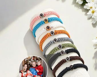 Peut inclure: Une pile de huit bracelets tressés colorés avec une perle noire et un accent doré sur chacun. Les bracelets sont disposés en cercle sur une surface blanche.