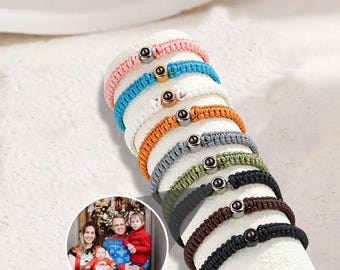 Peut inclure: Plusieurs bracelets en macramé de différentes couleurs : rose, bleu, blanc, orange, gris, vert, marron et noir. Chaque bracelet est orné d'une perle sombre et ronde. Les bracelets sont présentés sur une surface blanche texturée.