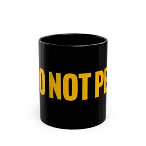 Könnte beinhalten: Schwarze Keramiktasse mit dem Text "Do Not Pet" in gelben Buchstaben.