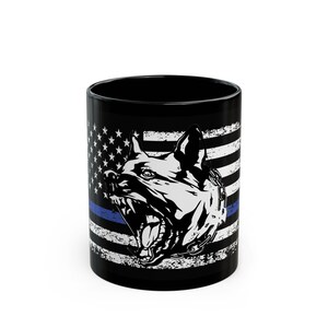 May include: Black ceramic mug with a white and blue American flag design. A black and white illustration of a dog's head with a chain collar is in the center of the flag. A thin blue line is across the bottom of the flag.