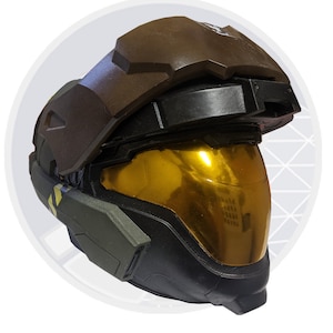 May include: A replica futuristic helmet with a dark brown upper section and a gold-tinted visor. The helmet has a black base with olive green accents and yellow markings. The design suggests a science fiction or gaming theme.