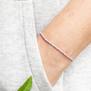 May include: A pink and blue friendship bracelet on a person's wrist.