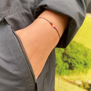 Könnte beinhalten: Eine schwarze Jacke mit einer Reißverschlusstasche und einem schwarzen Armband mit bunten Perlen.