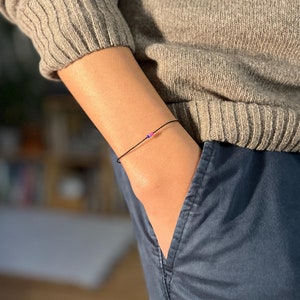 Könnte beinhalten: Ein schwarzes Armband aus Schnur mit einer kleinen rosa und blauen Perle.