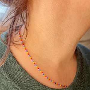 Op de afbeelding: Een kleurrijke kralenketting met rode, oranje, gele, groene, blauwe en paarse kralen. De ketting wordt gedragen door een persoon met bruin haar.