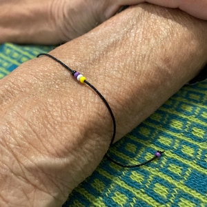 Könnte beinhalten: Ein schwarzes Armband mit einem kleinen Anhänger aus lila, weißen und gelben Perlen.